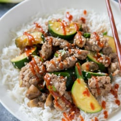 A close up of the stir fry over rice in a white bowl.