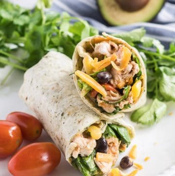 Two BBQ Chicken Salad Wraps on a white plate with grape tomatoes and cilantro.