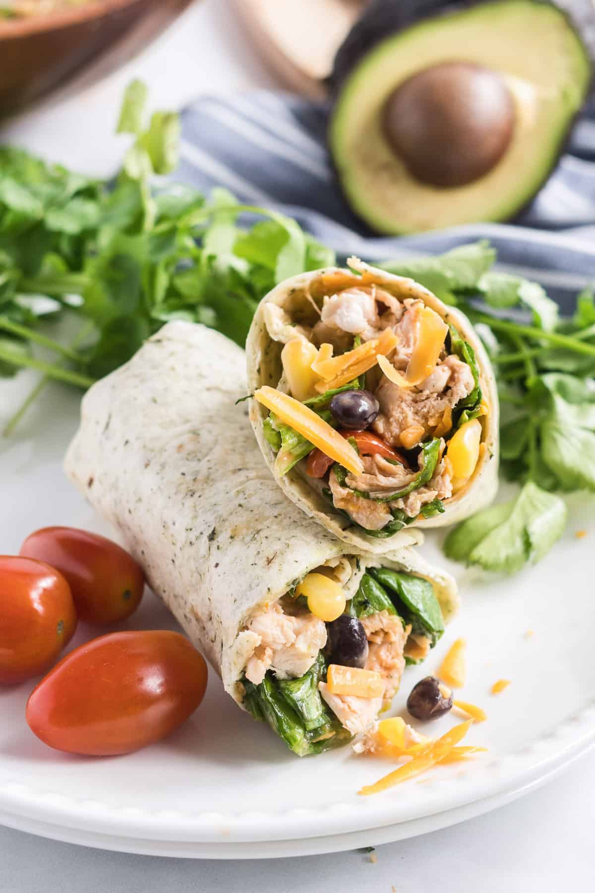 A BBQ Chicken Salad Wrap cut in half and stacked on a white plate with grape tomatoes and cilantro.