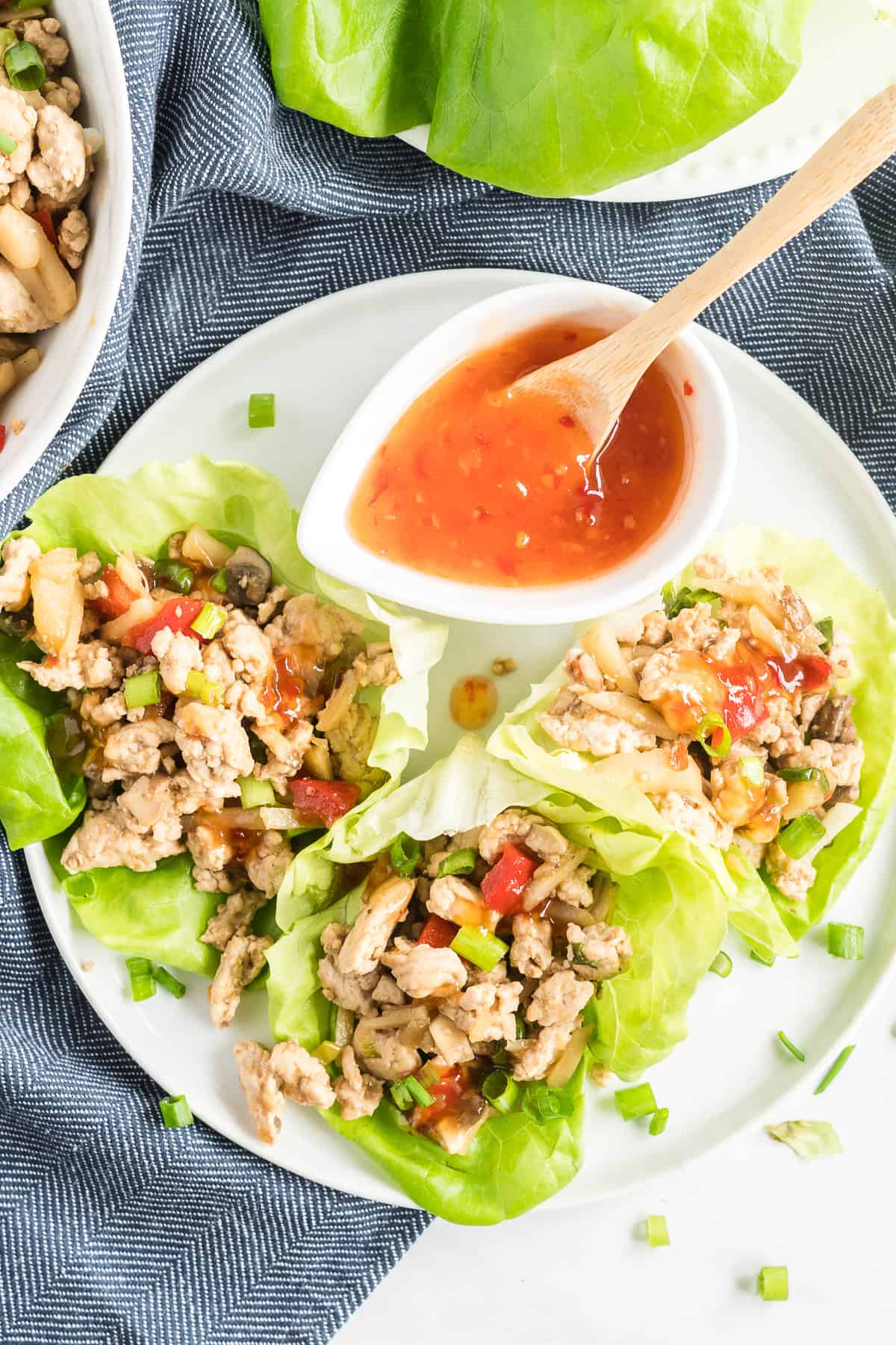 Three Chicken Lettuce Wraps on a white plate with sweet chili sauce shot from over the top.