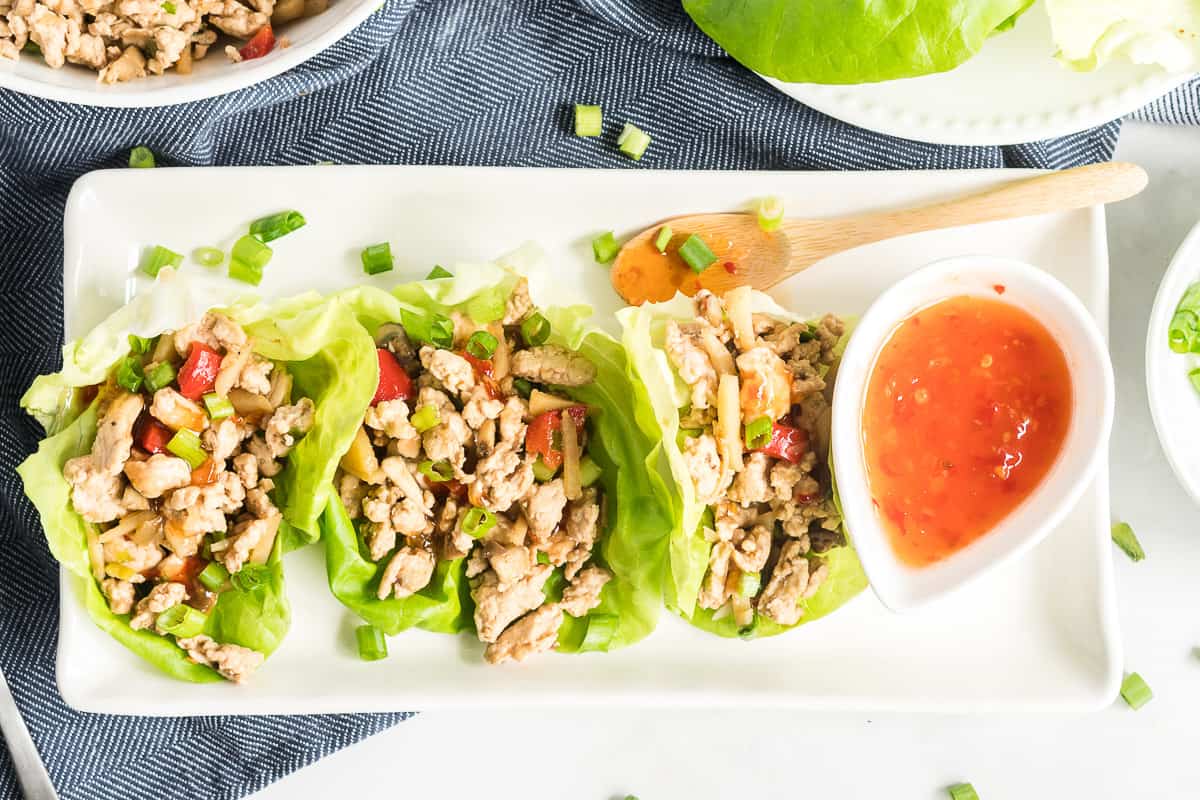 Three Chicken Lettuce Wraps on a white tray with sweet chili sauce.