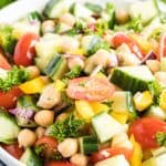 A close up of the salad with chickpeas, cucumbers, and tomatoes in a white serving bowl.