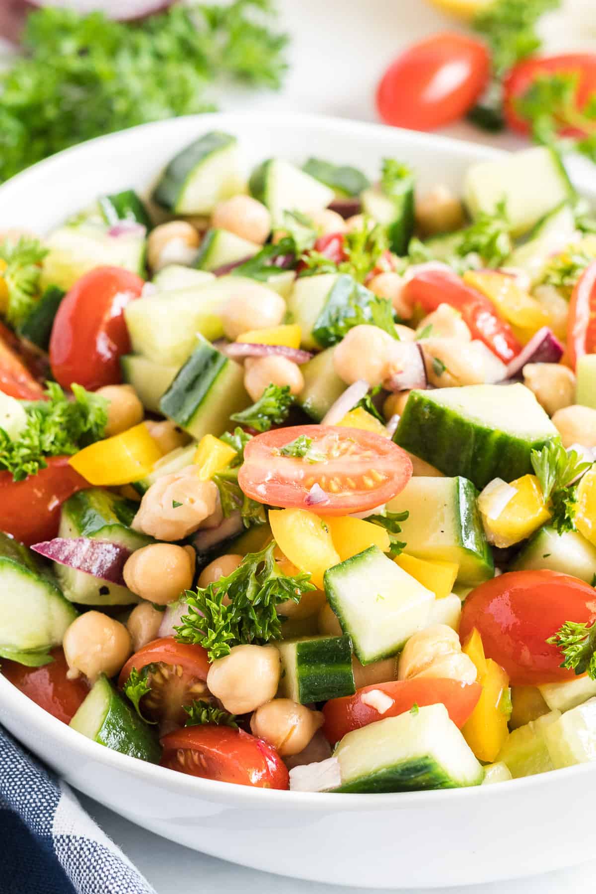 A close up of the salad with chickpeas, cucumbers, and tomatoes in a white serving bowl.