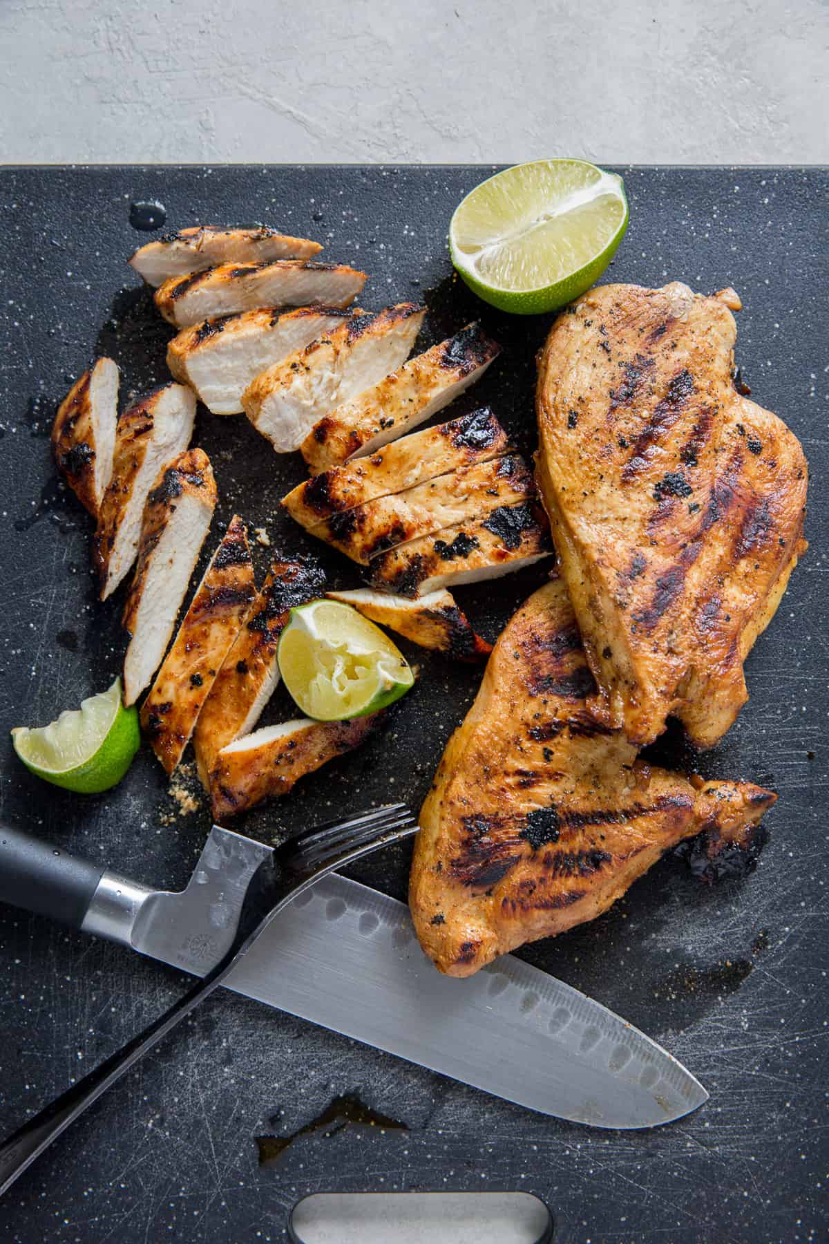 Pieces of sliced grilled chicken on a black cutting board with a knife.