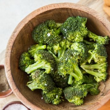 Steamed broccoli in a wood bowl with an orange napkin and salt to the side