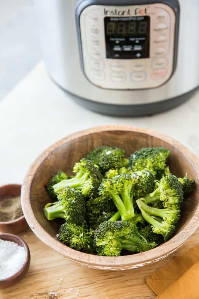 Steamed broccoli in a wood bowl with an orange napkin with an Instant Pot in the background