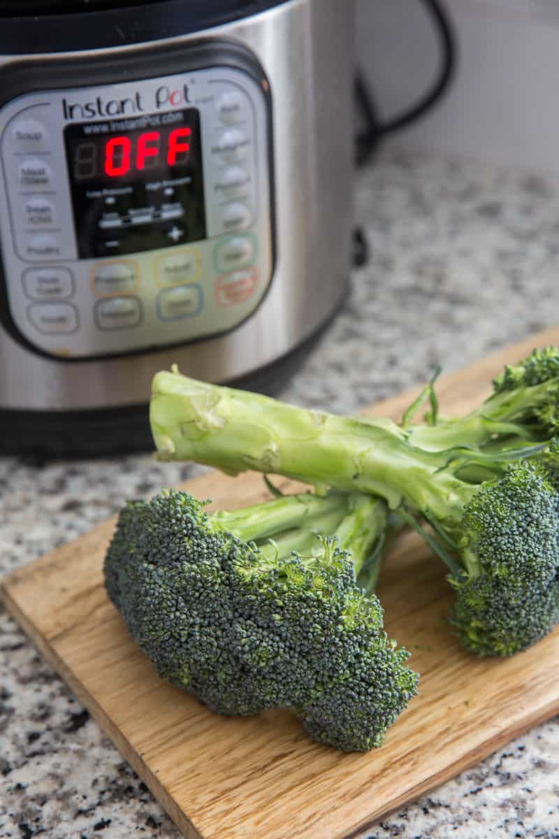 2 heads of broccoli on a cutting board with an Instant Pot in the background