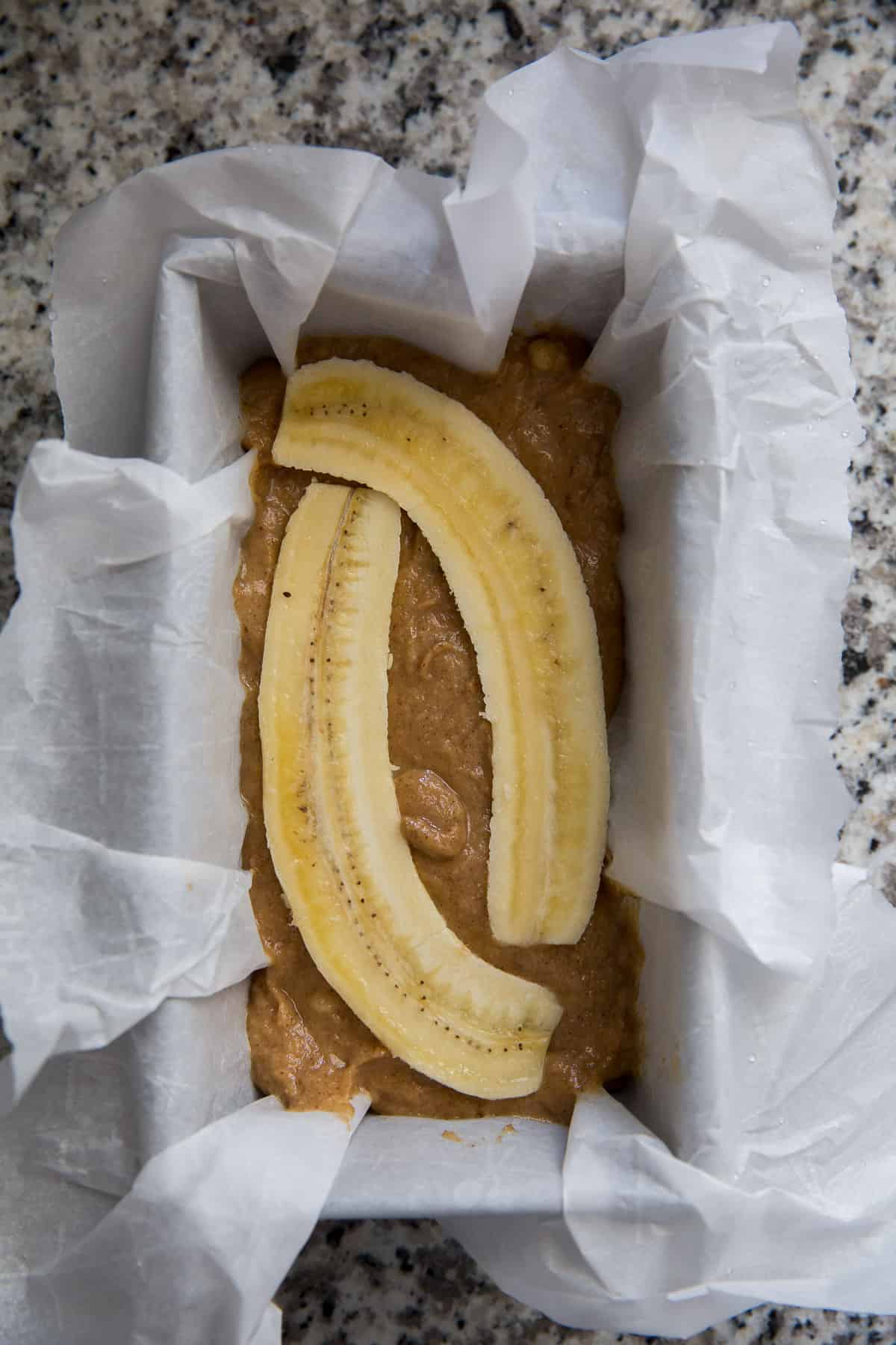 banana bread batter in a pan lined with parchment topped with a sliced banana