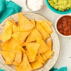 air fryer tortilla chips on a plate with salsa , guacamole and sour cream on the side in bowls.