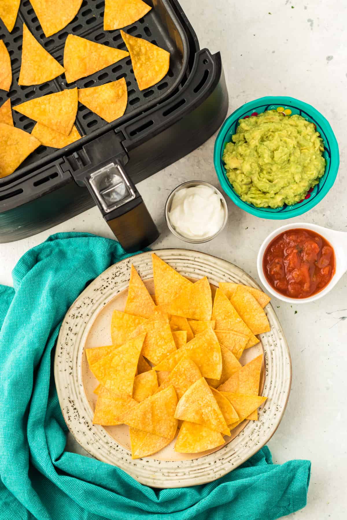 Air fryer tortilla chips on a plate with sour cream, guacamole and salsa in bowls on a table.