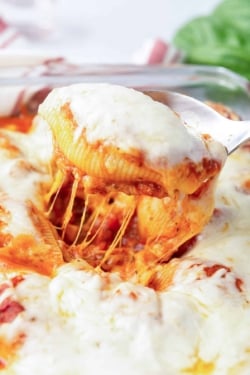 A spoon lifts a cheesy stuffed pasta shell from a dish.