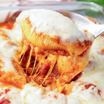 A spoon lifts a cheesy stuffed pasta shell from a dish.