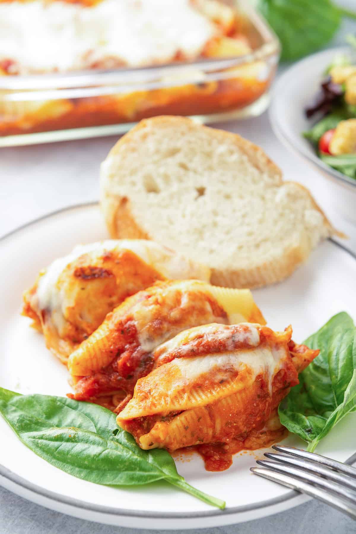 Three stuffed pasta shells topped with marinara and cheese on a white plate.