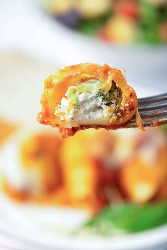 A fork lifts a piece of a pasta shell stuffed with broccoli and cheese.