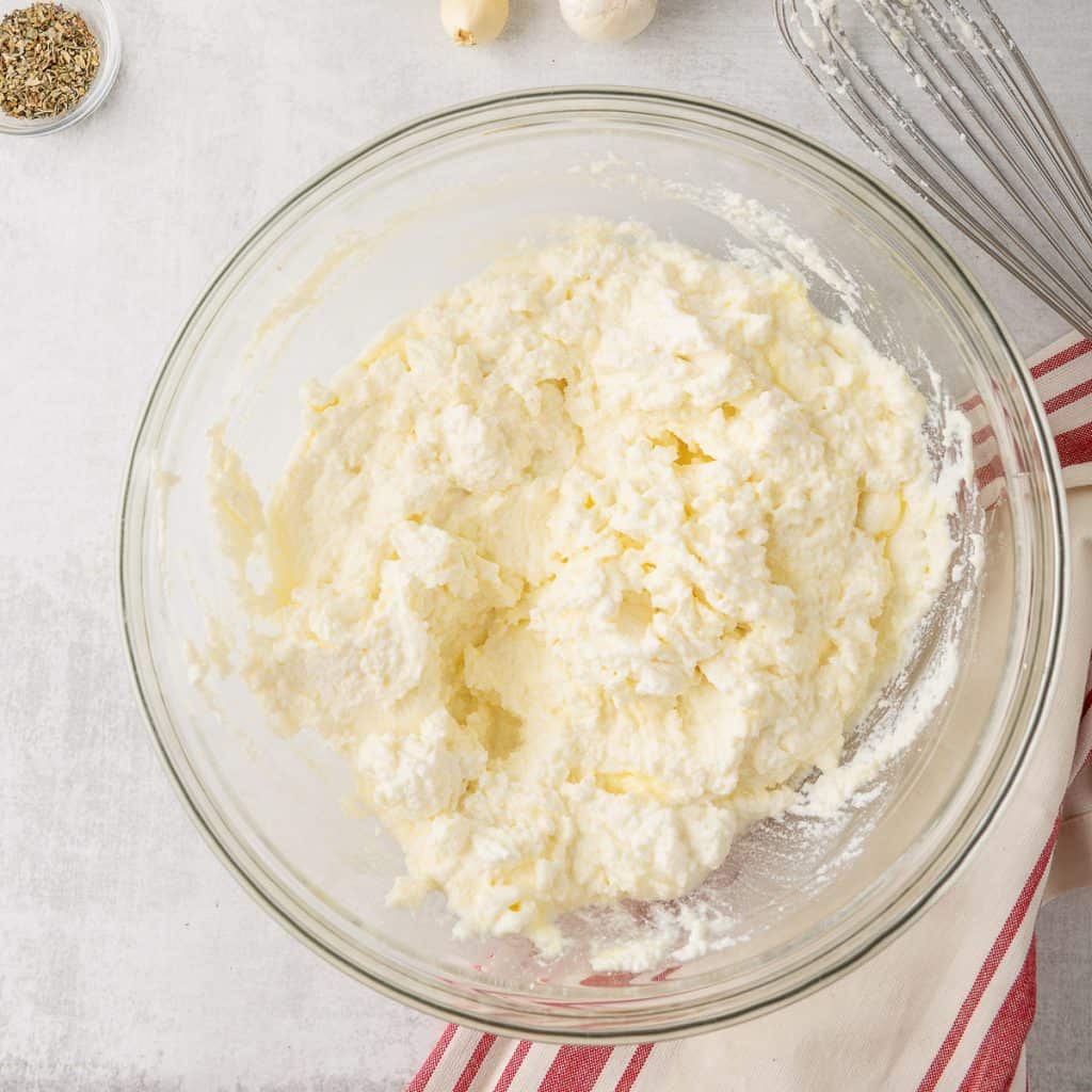 Ricotta cheese mixed with eggs in a glass bowl.