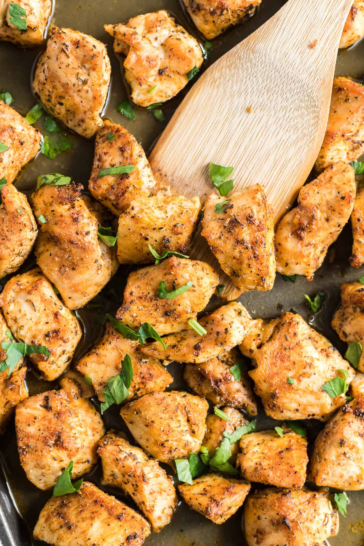 Small pieces of cooked chicken on a baking sheet topped with parsley.