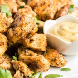 Seasoned, cooked bites of chicken on a plate with a small bowl of Dijon mustard.