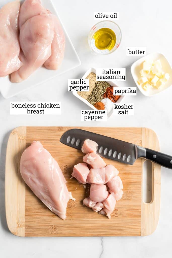 Boneless chicken, spices, olive oil and butter on a white counter with text overlay.