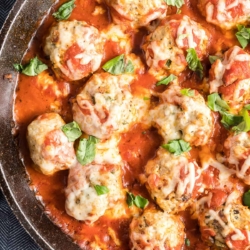 A skillet filled with meatballs with marinara and melted cheese.