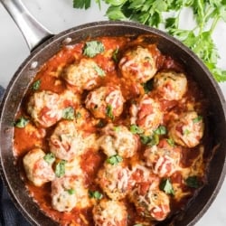 A skillet filled with meatballs topped with marinara and melted cheese.