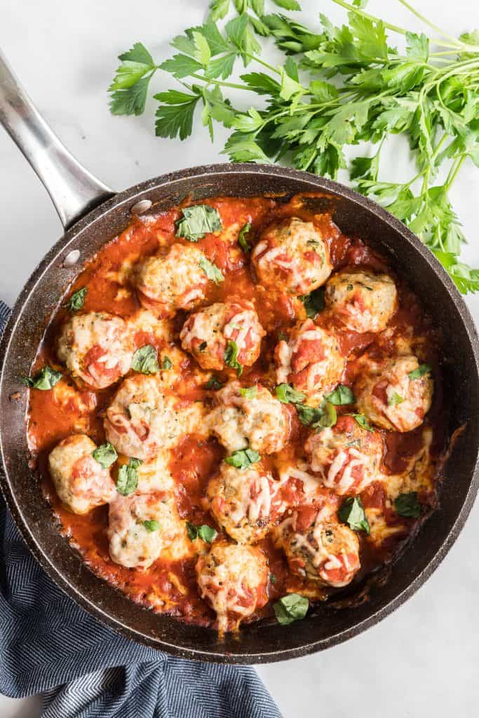 A skillet filled with meatballs topped with marinara and melted cheese.