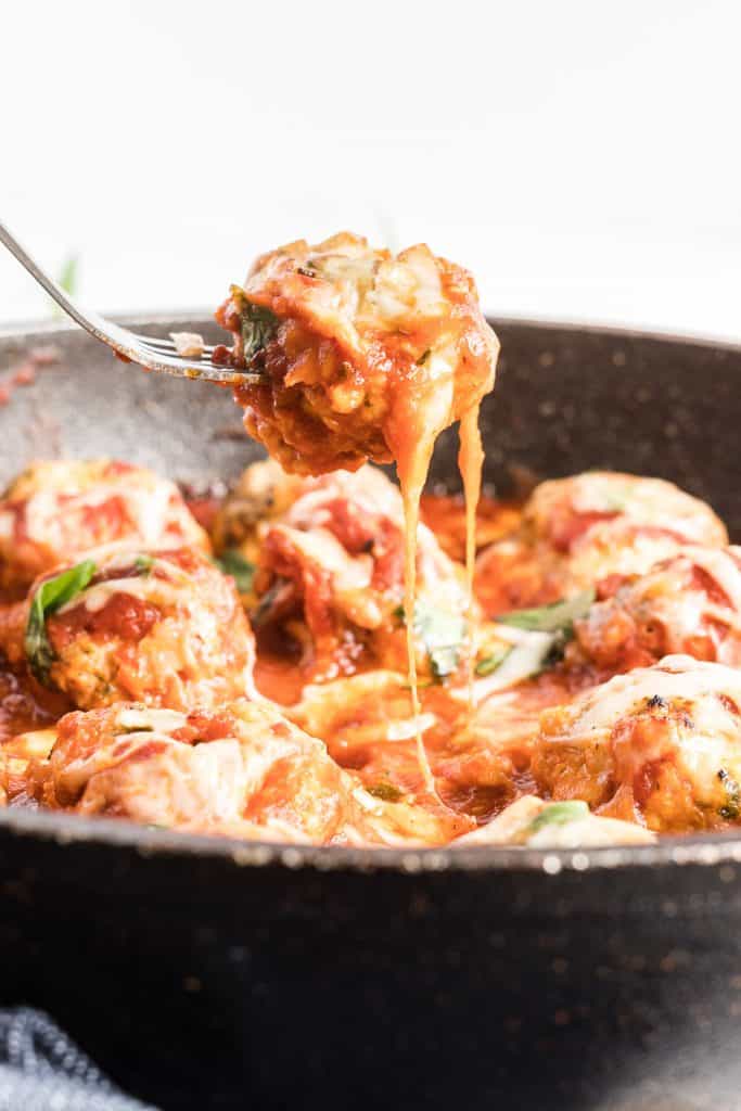 A fork lifts a meatball from a skillet.