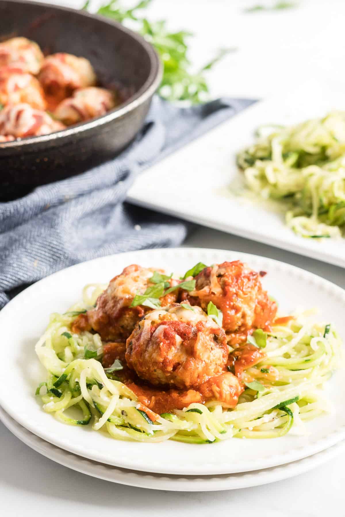 Three turkey meatballs on top of zucchini noodles on a white plate.