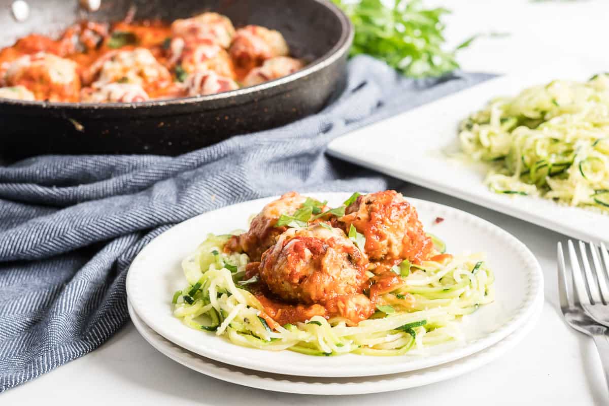 Three meatballs on top of zucchini noodles on a white plate.