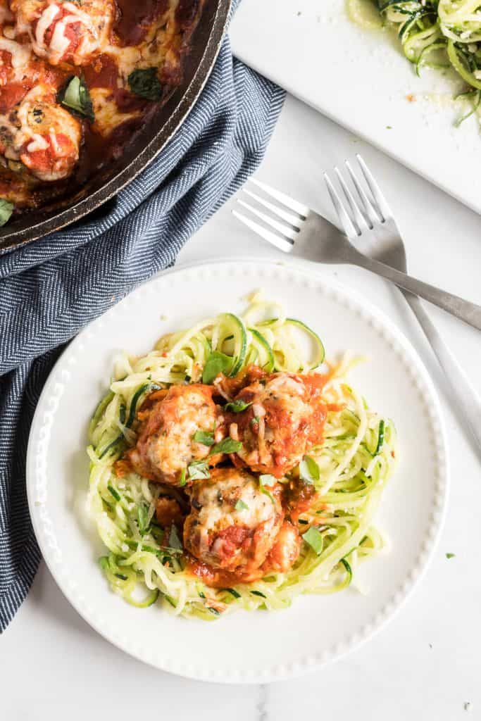 Three turkey meatballs over zucchini noddles on a white plate shot from over the top.