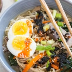 Ramen in a bowl with a soft boiled egg and chopsticks.