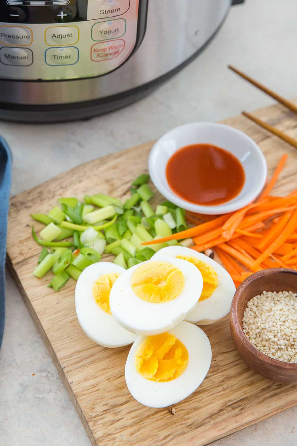 Soft boiled eggs sliced in half on a cutting board with carrots and green onions.