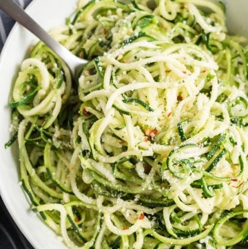 A white bowl filled with zoodles and a fork.
