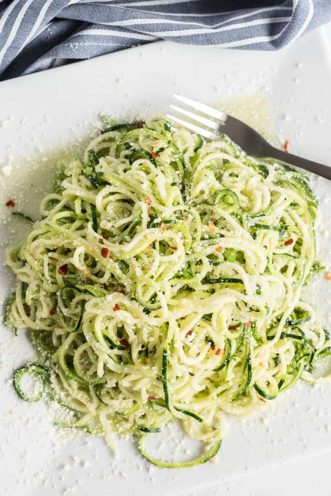 Zucchini noodles topped with Parmesan cheese on a white plate.
