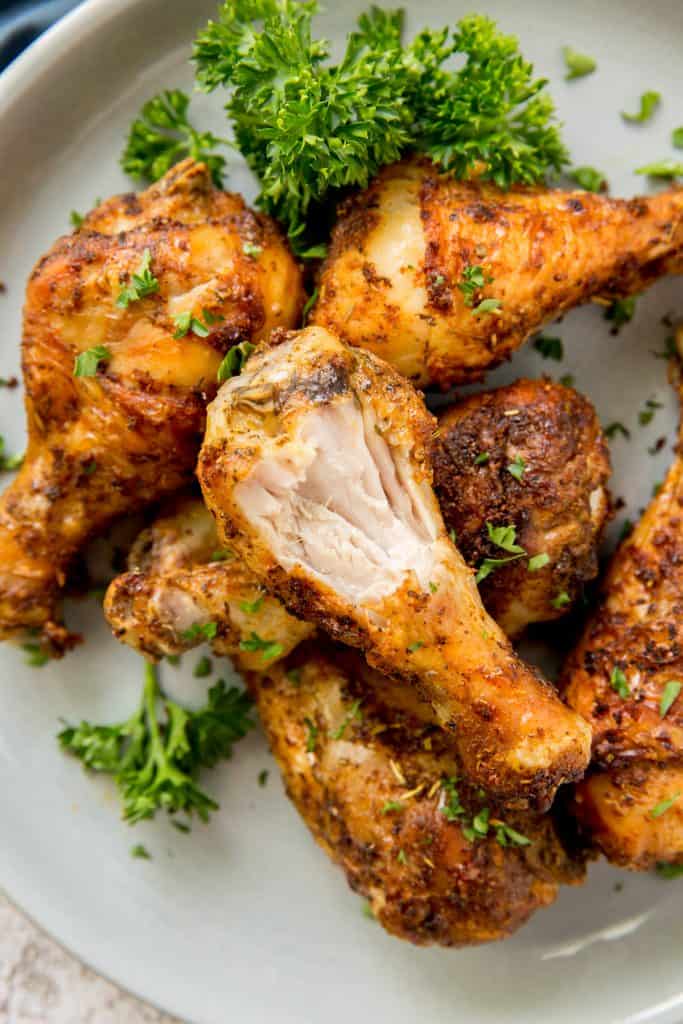 cooked chicken legs on a plate garnished with parsley and a bite taken out of one