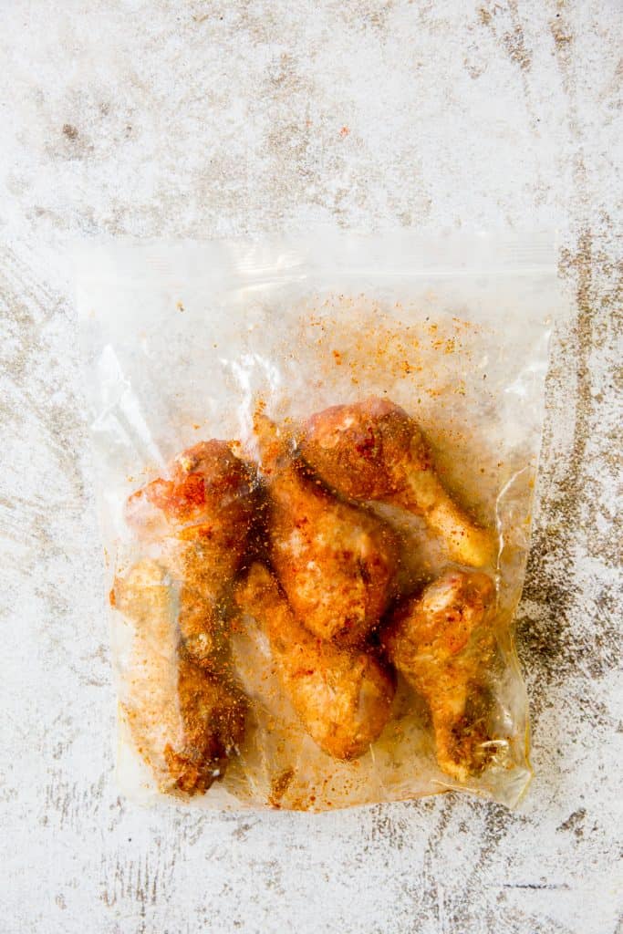 raw chicken legs seasoned in a gallon sized plastic bag