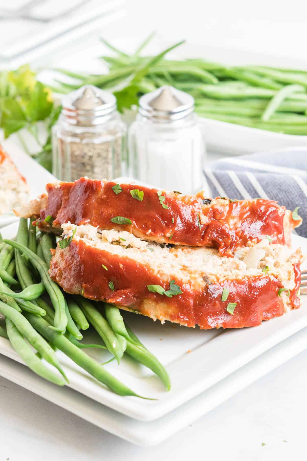 Two slices of meatloaf on a plate with green beans.