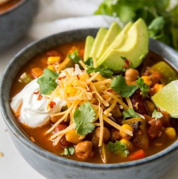 A bowl of chili with veggies topped with avocado, cheese and sour cream.