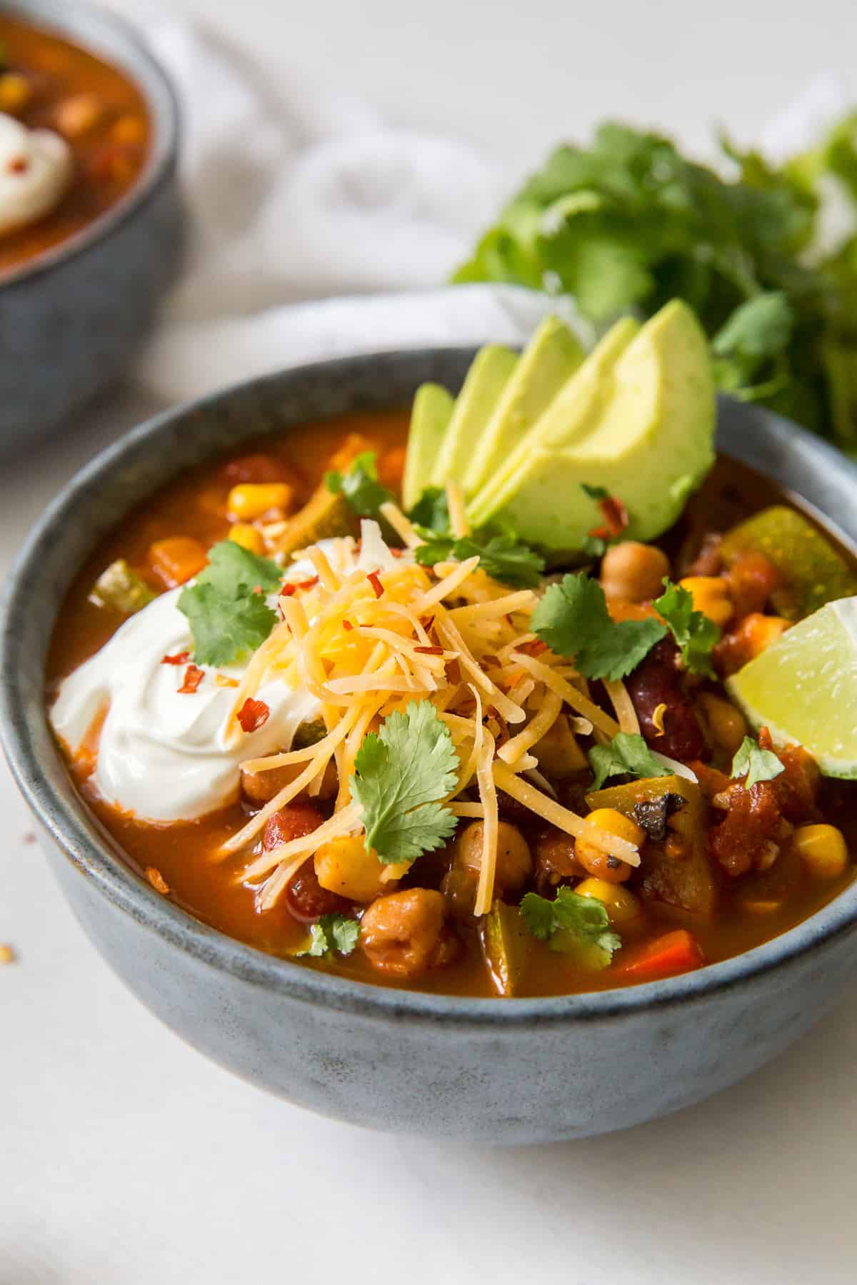 A bowl of chili with veggies topped with avocado, cheese and sour cream.
