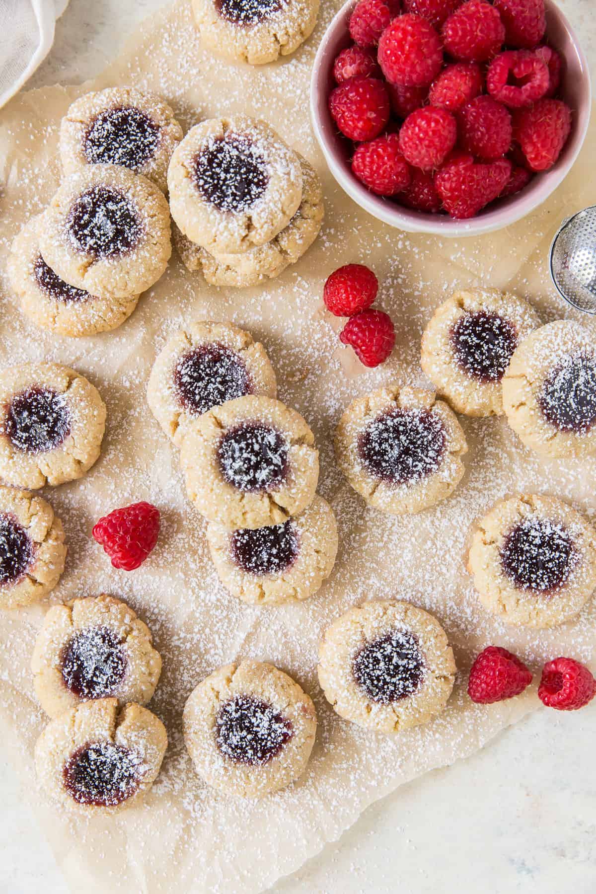 Thumbprint cookies dusted with powdered sugar next to a bowl of raspberries.