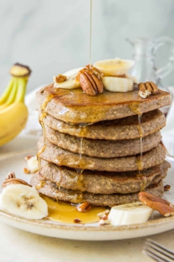 Maple syrup pouring over a stack of Banana Oat Pancakes.