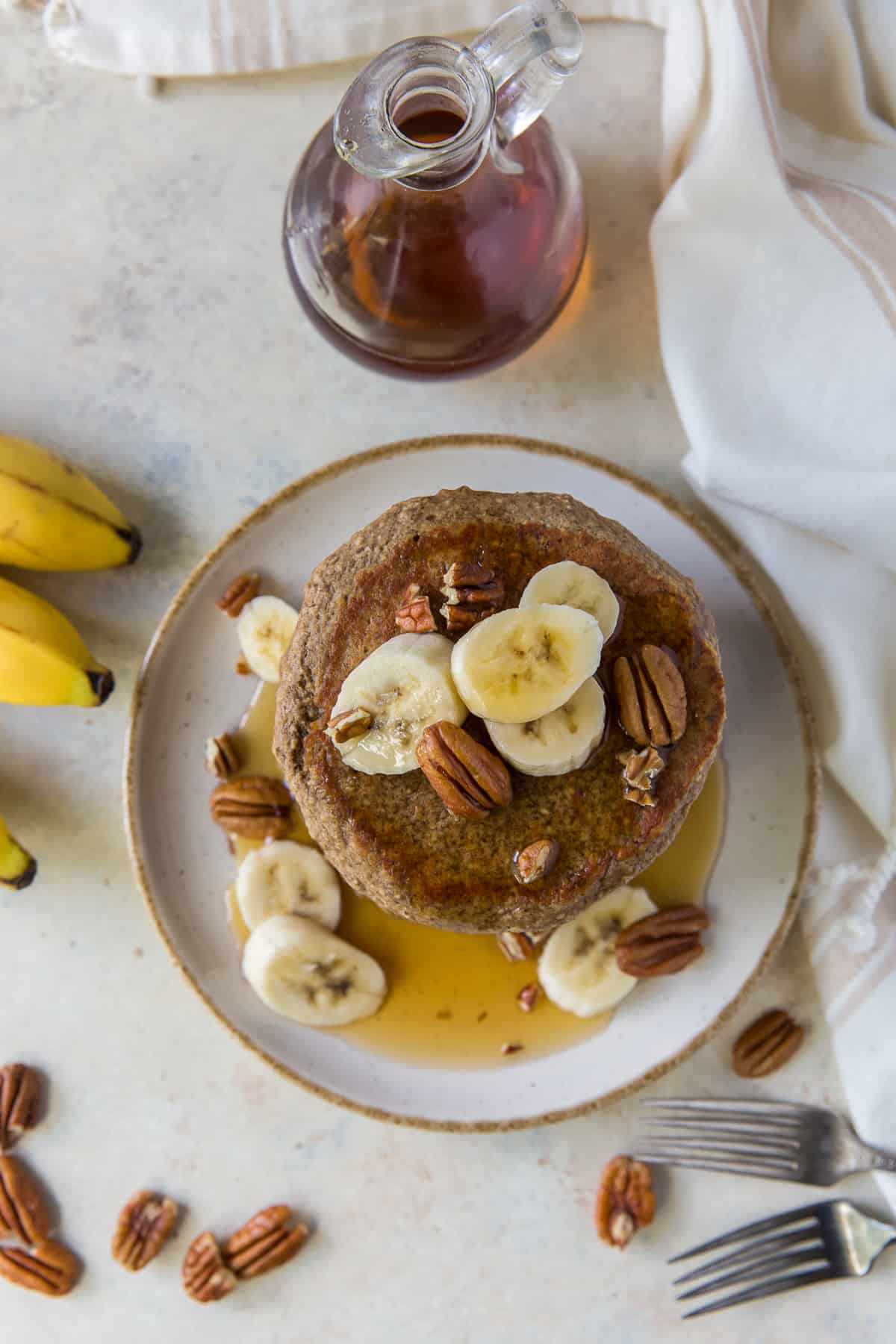 A stack of pancakes topped with bananas and pecans shot from over the top.