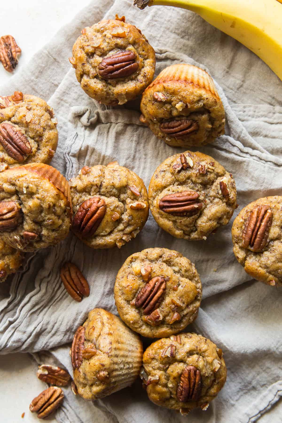 Muffins topped with pecans piled on a grey cloth.