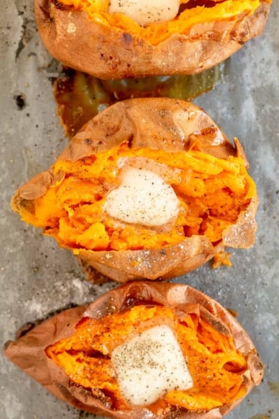Three baked sweet potatoes topped with butter shot from over the top.