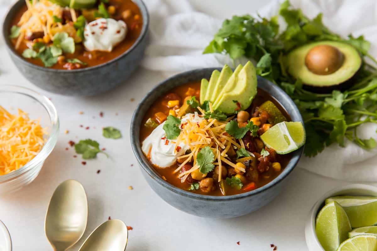 Two bowls of chili with toppings with cilantro and an avocado nearby.