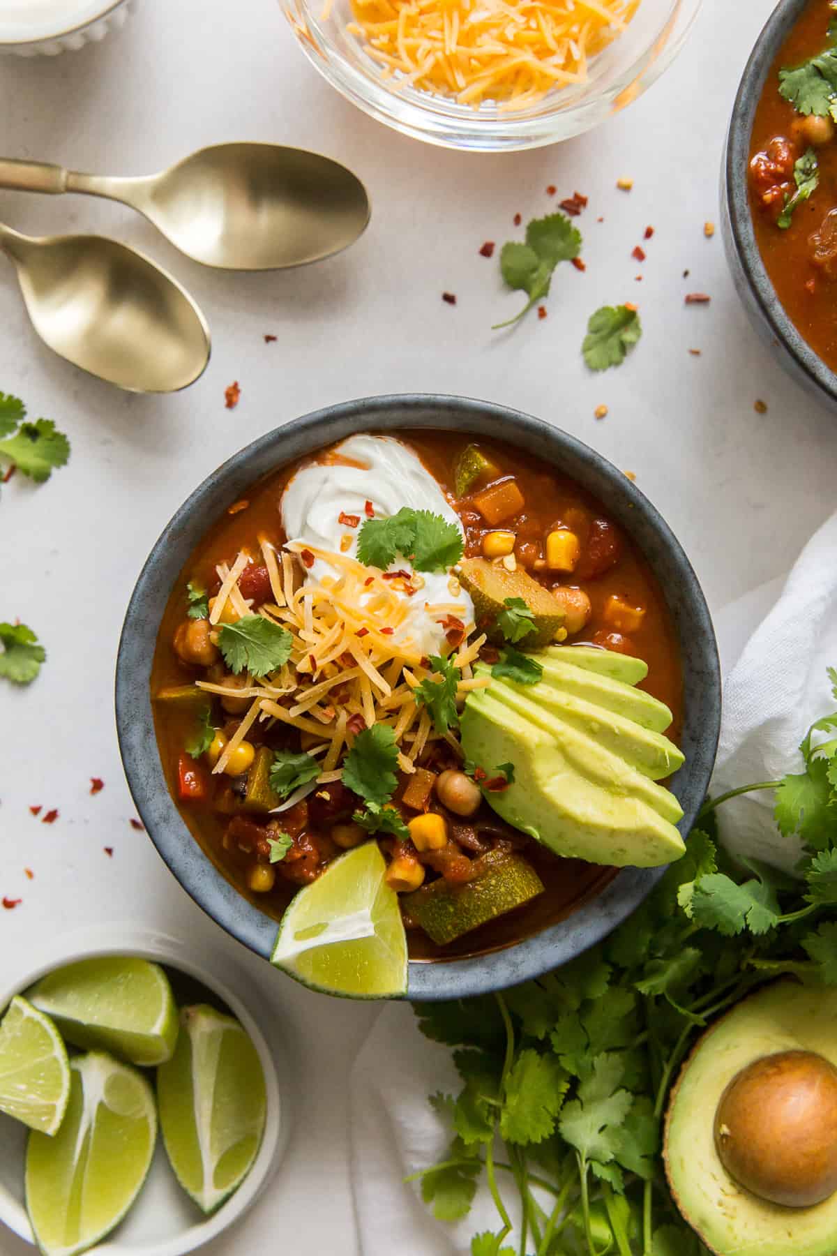 A bowl of chili with slices of lime and spoons nearby.