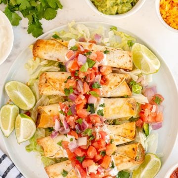 A platter of taquitos topped with pico de gallo shot from over the top.