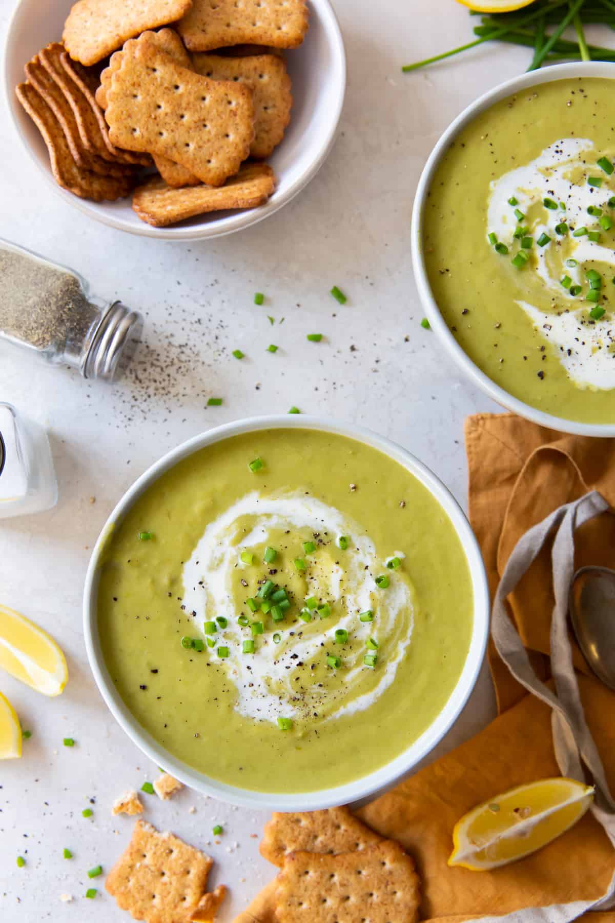 Two bowls of Asparagus Soup next to a bowl of crackers.