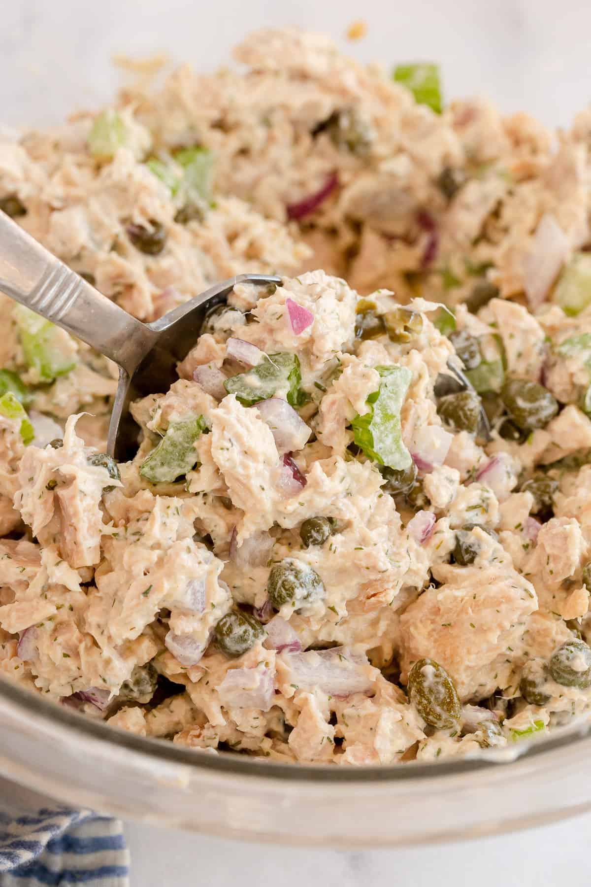 A close up of a spoon scooping tuna salad in a large bowl.