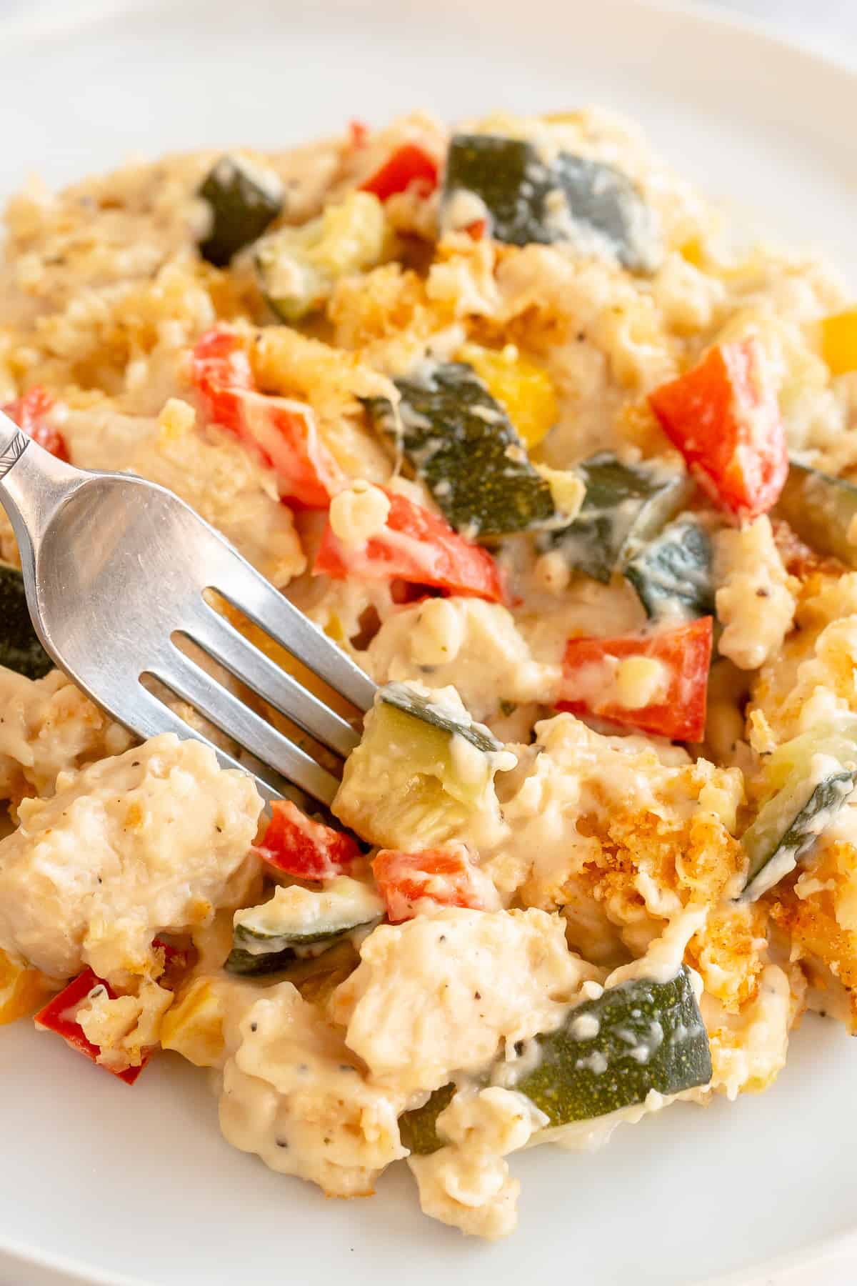 A fork digs into a serving of Chicken and Zucchini Casserole on a white plate.