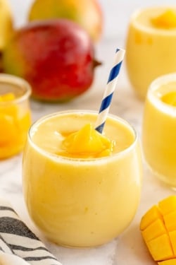 A mango smoothie in a small glass with a blue and white straw.